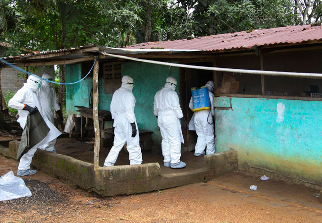 Enfermeros entran a una casa para proceder a trasladar el cuerpo de una víctima del virus Ébola hasta un sitio para enterrarle, en la comunidad de Banjor, a las auferas de Monrovia (Liberia). Foto: EFE