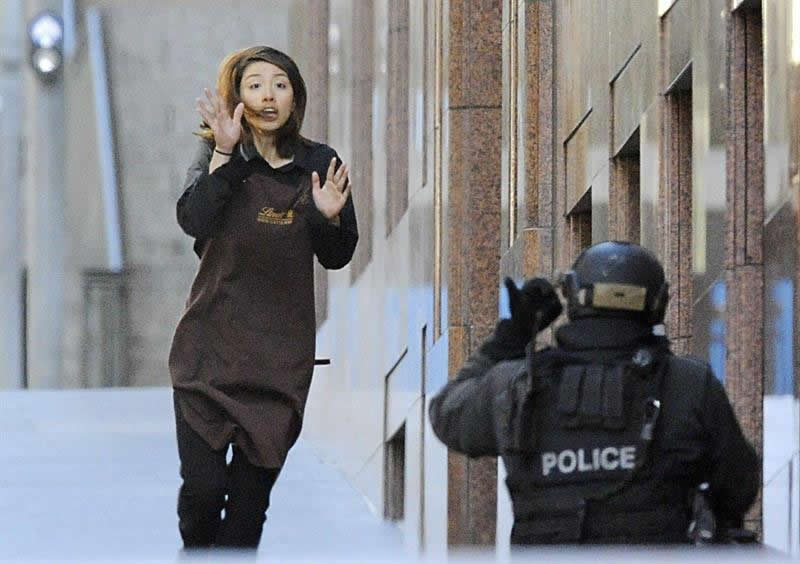 Una empleada abandona la cafetería donde trabaja y que un hombre armado tiene tomada desde primeras horas de la mañana en Sídney (Australia). Foto: EFE