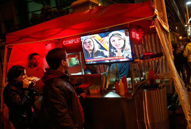 Personas siguen desde un puesto de comida callejero la transmisión de la primera noche del Festival Internacional de la Canción de Viña del Mar 2015. Foto: EFE